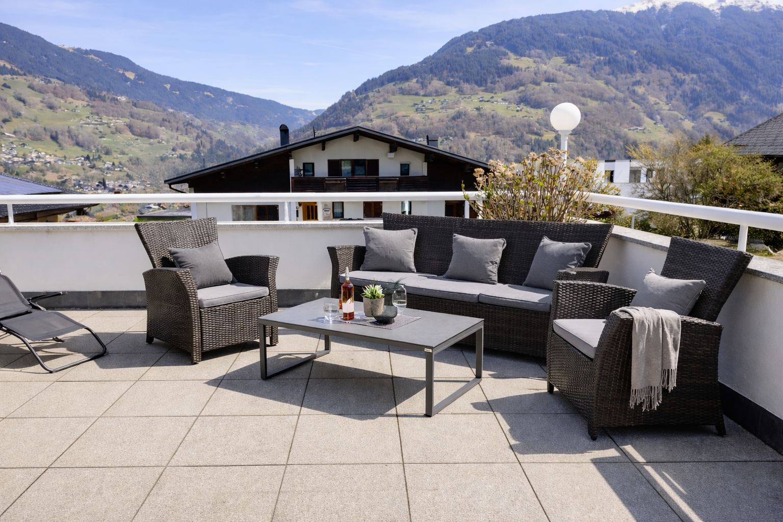 Terrasse Ferienwohnung Haus Bergharmonie Tschagguns Montafon – Lounge mit Rattanmöbeln, Rosé und schneebedecktem Bergpanorama