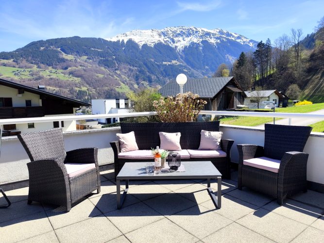 Terrasse Ferienwohnung Haus Bergharmonie Tschagguns – Lounge mit Rattanmöbeln und schneebedecktem Bergpanorama Montafon